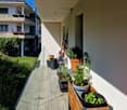 Balcony with potted plants, gardening tools, and wooden planters. Exterior view of apartment building with white walls and balconies.