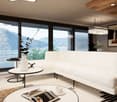 Spacious living room with large windows offering a scenic view of the mountains and lake. The room features a white sofa, coffee table, and decorative accents. The ceiling has wooden beams and recessed lighting. Overall, the space has a modern and cozy am