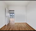 Empty room with white walls, hardwood flooring, and a doorway leading to another room.