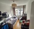 wooden floor, bed, desk, laptop, clothes hanging and various items on shelves