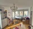 large room with large windows, balcony, dining table, dining chairs, shelves, toys, chandelier