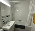 White bathtub, white tiled walls, white sink, mirror, built-in cabinet, private washing machine