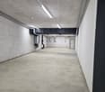 Empty parking area with concrete floor, white walls, and ceiling with lights and pipes.