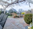 Stone patio, metal chairs, hanging plant, potted plants, garden table, frog statue, pergola