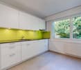 white cabinets, yellow backsplash, granite countertops, stainless steel sink, faucet, power outlet, white radiator, windows with trees view