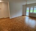 Empty room with wooden parquet floor, sliding door, balcony, white walls, power outlets.