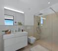 modern bathroom with white tile, white vanity, modern shower, toilet, towel rack