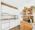Rustic kitchen with white cabinets, wooden beams, tiled backsplash, stainless steel appliances including a dishwasher, and a wooden storage cabinet with shelves and drawers