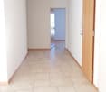 Empty hallway with beige tile, white walls, wooden door, light fixtures on the ceiling