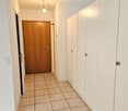 Lighted hallway, brown wooden door, white wardrobes, tiled flooring