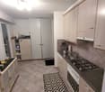 Modern kitchen with tiled flooring, stainless steel sink, electric stove, cabinets, refrigerator, and storage unit.