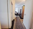 Empty hallway with white walls, dark floor, oriental rug, doorway leading to dining room