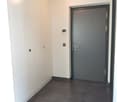 empty hallway, white walls, white doors, grey tiled floor, grey door, grey interior with silver handle and door knob, and white exterior with silver handles, thermostat, and light switch