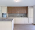 Open kitchen with island, marble counter, modern wooden cabinets, granite backsplash, gas stove, oven, granite countertops, stainless steel faucet, under-cabinet lighting, large glass door leading to a balcony.