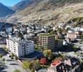 The image shows a panoramic view of a city nestled in a mountainous valley. The city is composed of a mix of residential and commercial buildings, with some high-rise apartment buildings visible. The surrounding landscape features terraced farmland and fo