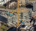 Aerial view of an ongoing construction site with multiple floors and several parked cars in front of the site.
