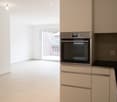 Empty room with glass door to the balcony, white cabinetry, stainless steel oven, tiled floor