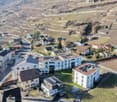 Aerial view of several terraced houses with solar panels on the roofs, built on the hillside of a valley. The neighborhood is surrounded by vineyards and has a beautiful view of the valley.