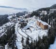 aerial view of mountain slope with wooden houses, roads, trees, and snow