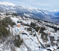 Aerial view of ongoing construction in a mountainous region, surrounded by snow, with mountains in the background.