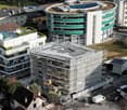 Aerial view of a building complex under construction with multiple stories, green roofs, and scaffolding.
