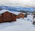 Two wooden chalets under construction with a beautiful snowy view of the mountains