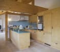 Open concept kitchen with wooden walls and ceiling, kitchen island with blue countertop, built-in appliances, and a fireplace in the background.