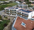 Aerial view of a modern apartment complex with solar panels on the roofs, a swimming pool on the terrace, and a construction site in front.