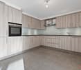Spacious modern kitchen with gray wood-paneled cabinets, built-in oven, and gray tile flooring