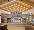 Spacious open-concept living room with high vaulted wooden ceiling, large windows offering a scenic mountain view, wooden floors, and leather furniture
