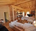 Spacious open-concept living area with wooden beamed ceiling, large windows, comfortable sofas, dining table, and a fireplace