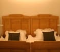 The image shows a bedroom with two wooden headboards, each with drawers and cabinets. The bed is made with white bedding and black accent pillows.