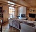 Cozy living room with wooden walls and ceiling, large windows, fireplace, TV stand, and comfortable sofa with a plush blanket