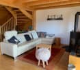 Cozy living room with wooden beams, white leather sofa, coffee table, and a fireplace. The room also has a staircase leading to an upper level.