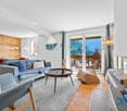 wooden wall, wooden floor, large windows, couch, coffee table, armchair, fireplace, balcony