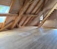 Spacious attic with exposed wooden beams and trusses, wooden flooring, and a staircase leading up to the space.