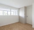 empty room with wooden floors, large windows, a power outlet, and an exit door