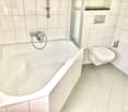 White tiles, bathtub, showerhead, toilet, toilet paper holder