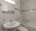 white tiles, white sink, white toilet, shower with handrail, mirror with shelf, bathtub