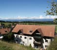 white building with brown roof, overlooking green valley, balcony on the second floor