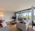 modern living room, grey sofa, black center table, TV, large windows with balcony
