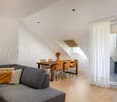 Open living area with a table and chairs, grey couch, white curtains, wooden floor, skylight, balcony