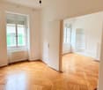 Empty room with wooden floors, white walls, large windows with white shutters, a radiator, and an open door.