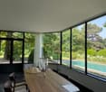 modern dining room with curved glass windows, wooden table, swimming pool outside