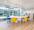 Empty meeting room with large table, yellow chairs, large windows, wooden floor, white walls, cabinets