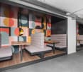 Modern and colorful office or cafe space with geometric wall mural, built-in seating, wooden tables, and hanging pendant lights.