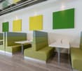 modern meeting area with green padded booths, white walls, square tables, yellow and green square wall decorations, potted plants