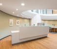 Reception area with arched ceiling, light hardwood floors, reception desk, round table, chairs, paintings on wall, green plants