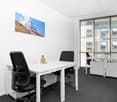 Bright and modern office space with large windows, white table, black office chairs, and a framed landscape image on the wall.