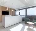 reception desk, chairs, round table, large windows, monitor on wall, wood and white color scheme